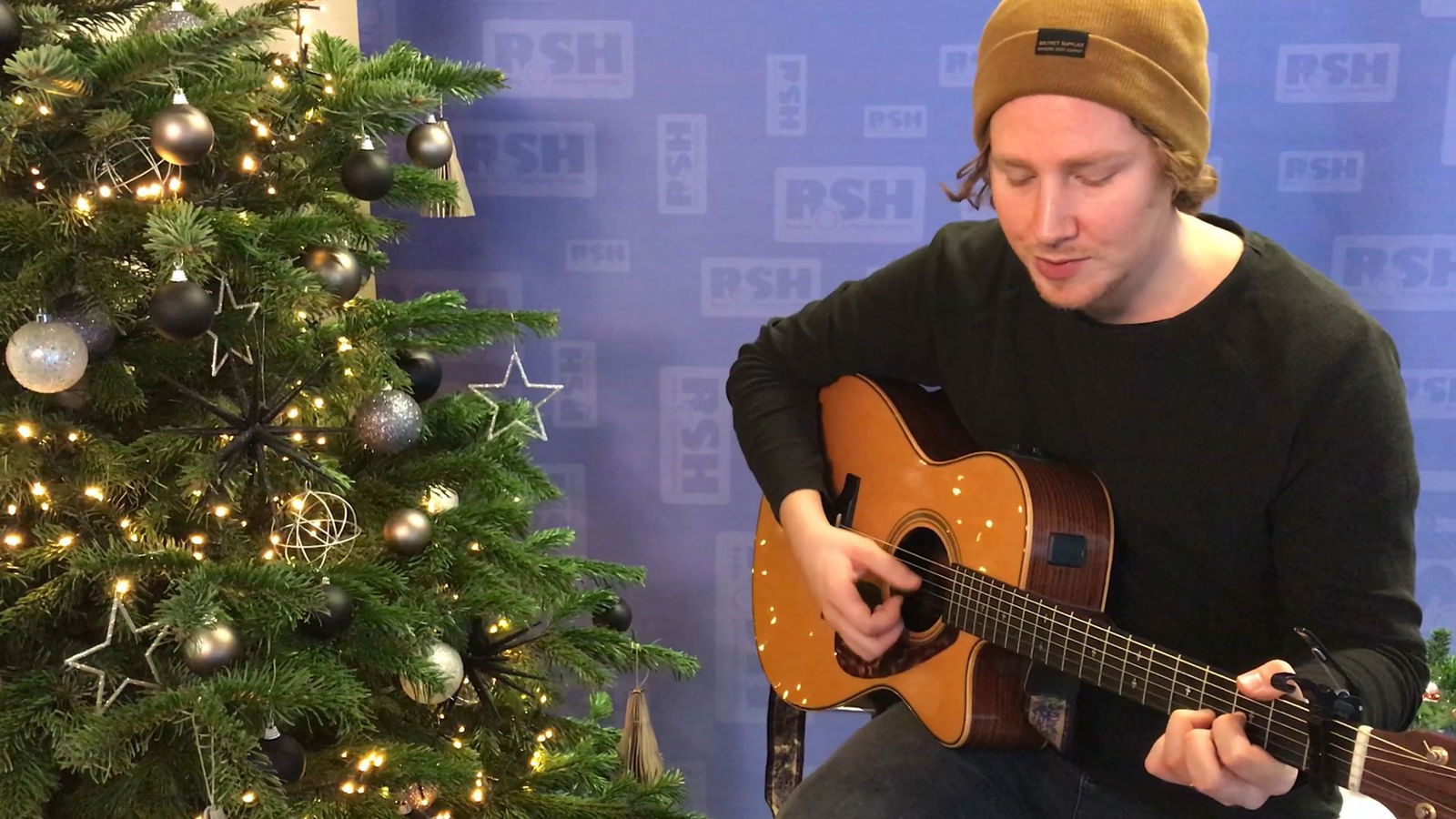 Michael Schulte spielt Gitarre vor einem Weihnachtsbaum.