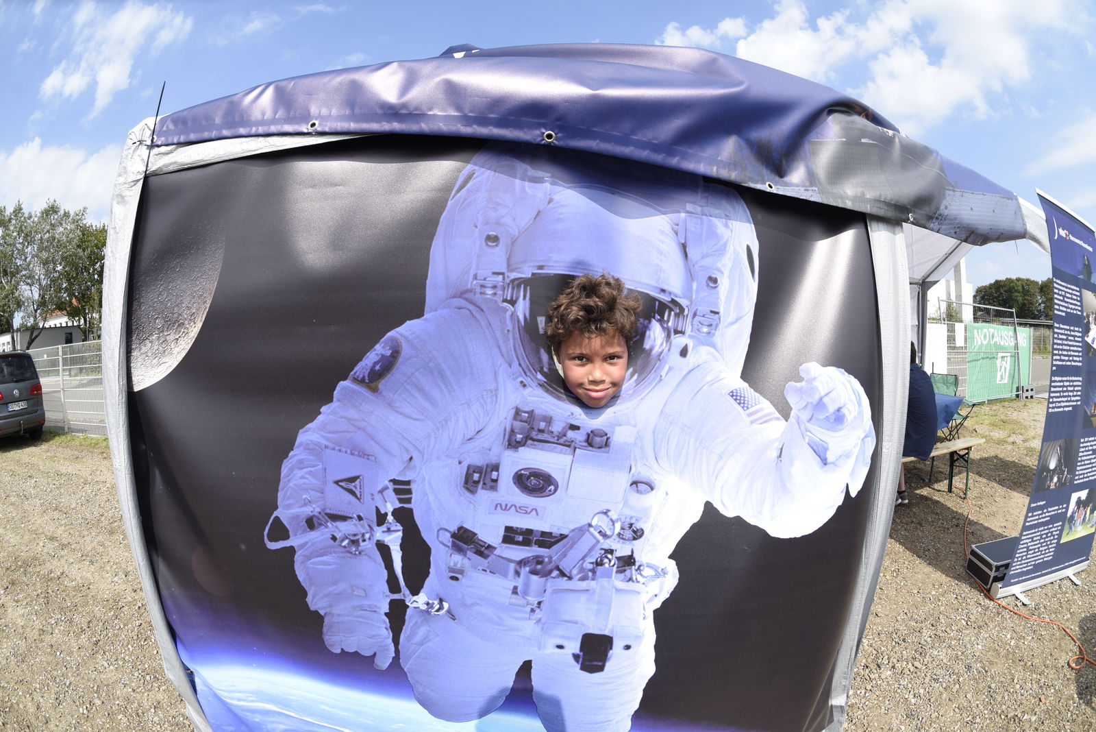 Ein Kind steckt den Kopf aus einer Fotoleinwand auf der ein Astronaut im Weltall abgebildet ist.