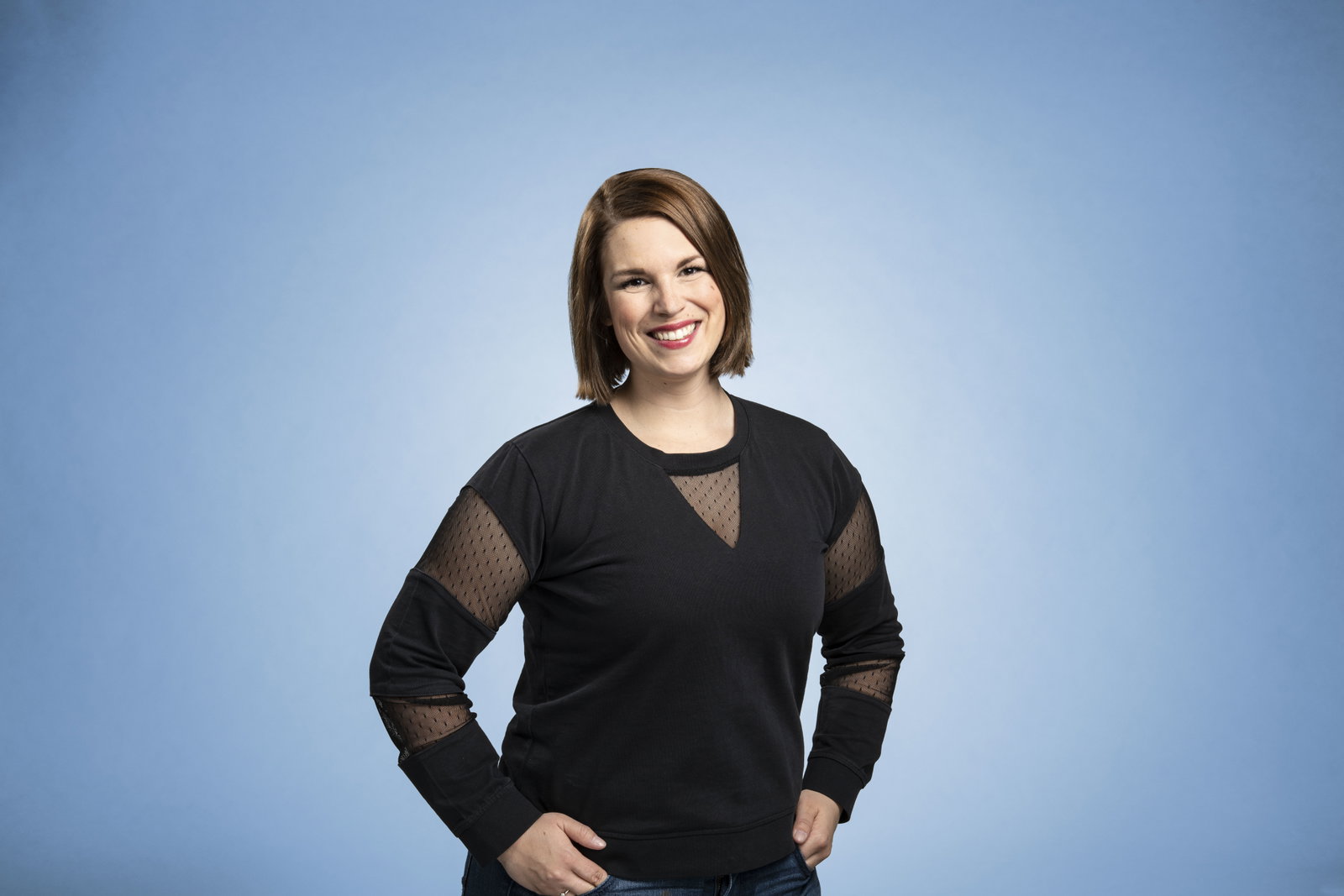 Carmen Wilkerling steht vor einem blauen Hintergrund und lächelt in die Kamera.