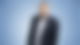 Carsten Kock steht vor einem blauen Hintergrund und guckt in die Kamera.