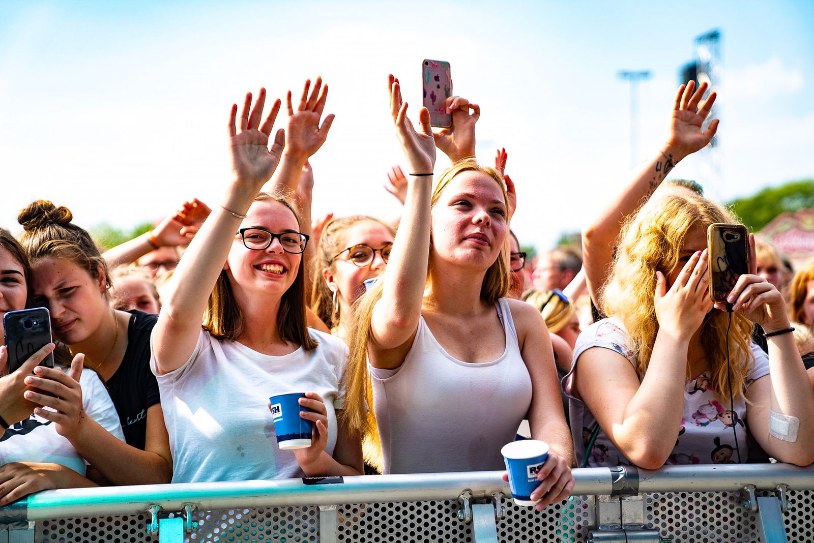 Mehrere junge Frauen stehen an einem Absperrgitter. Einige von ihnen heben die Hände in die Luft.Zwei von ihnen halten Smartphones hoch um ein Foto zu machen. 
