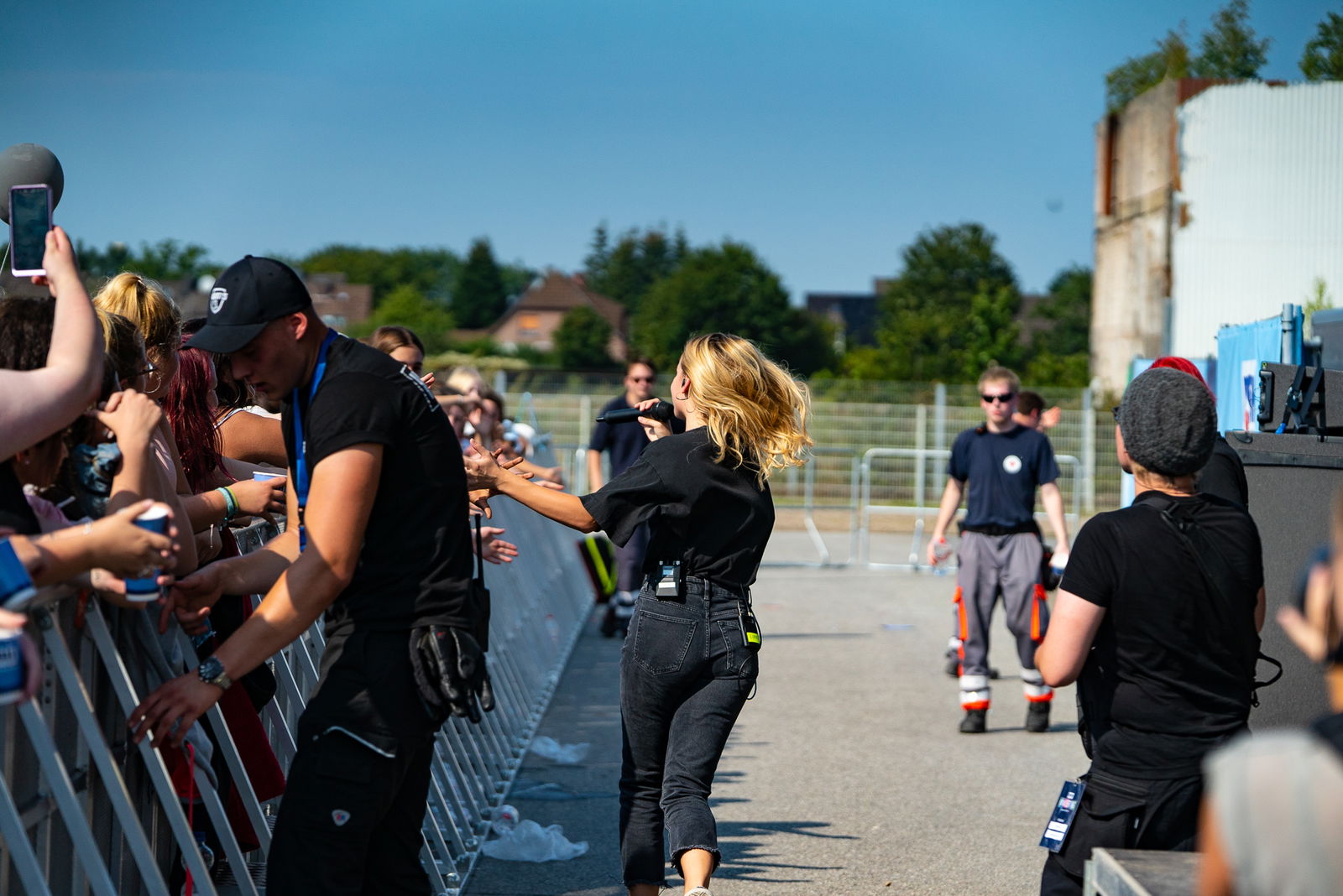 Eine Frau rennt durch einen Bühnengraben entlang einer Menschenmenge die hinter einer Absperrung steht und hält ihre Hand in Richtung der Menschenmasse.