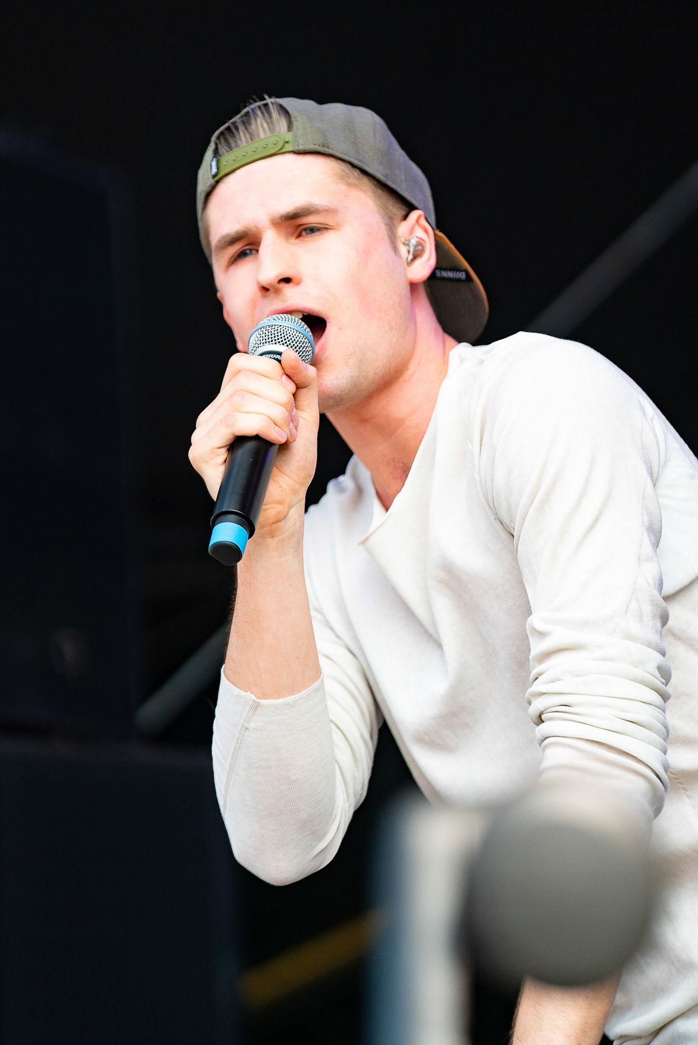 Ein junger Mann steht auf einer Bühne und singt in ein Mikrofon. 