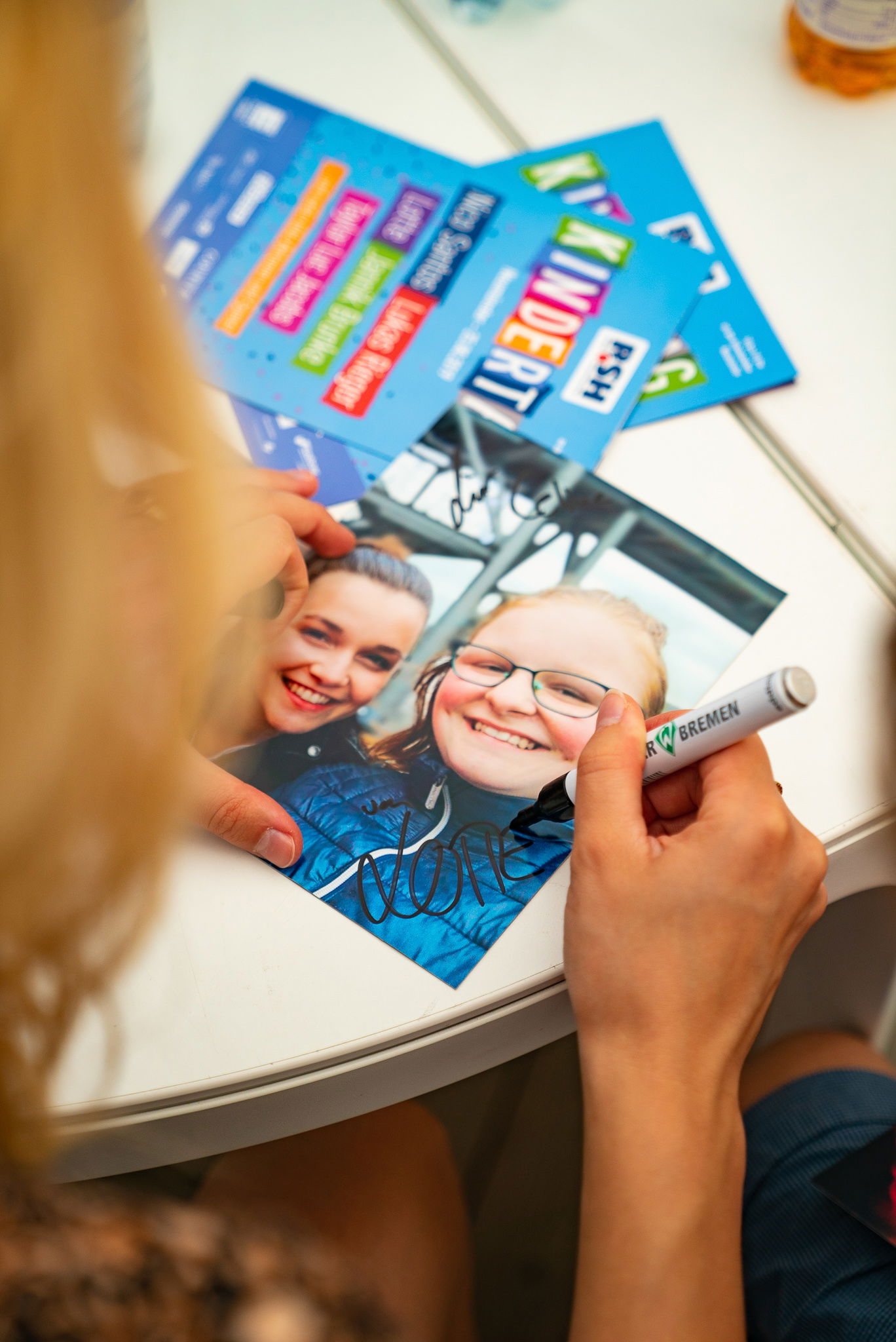 Eine Hand hält einen schwarzen Edding und schreibt ein Autogramm auf ein Bild auf dem zwei Frauen abgebildet sind.