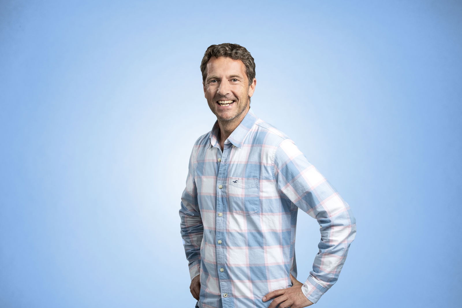 Voller Mittmann steht vor einem blauen Hintergrund und lächelt in die Kamera.