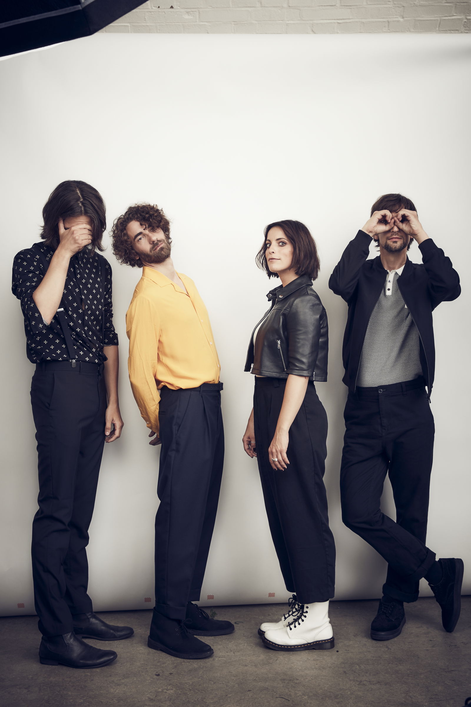 Drei Männer und eine Frau stehen vor einer weißen leinwand und gucken in die Kamera.