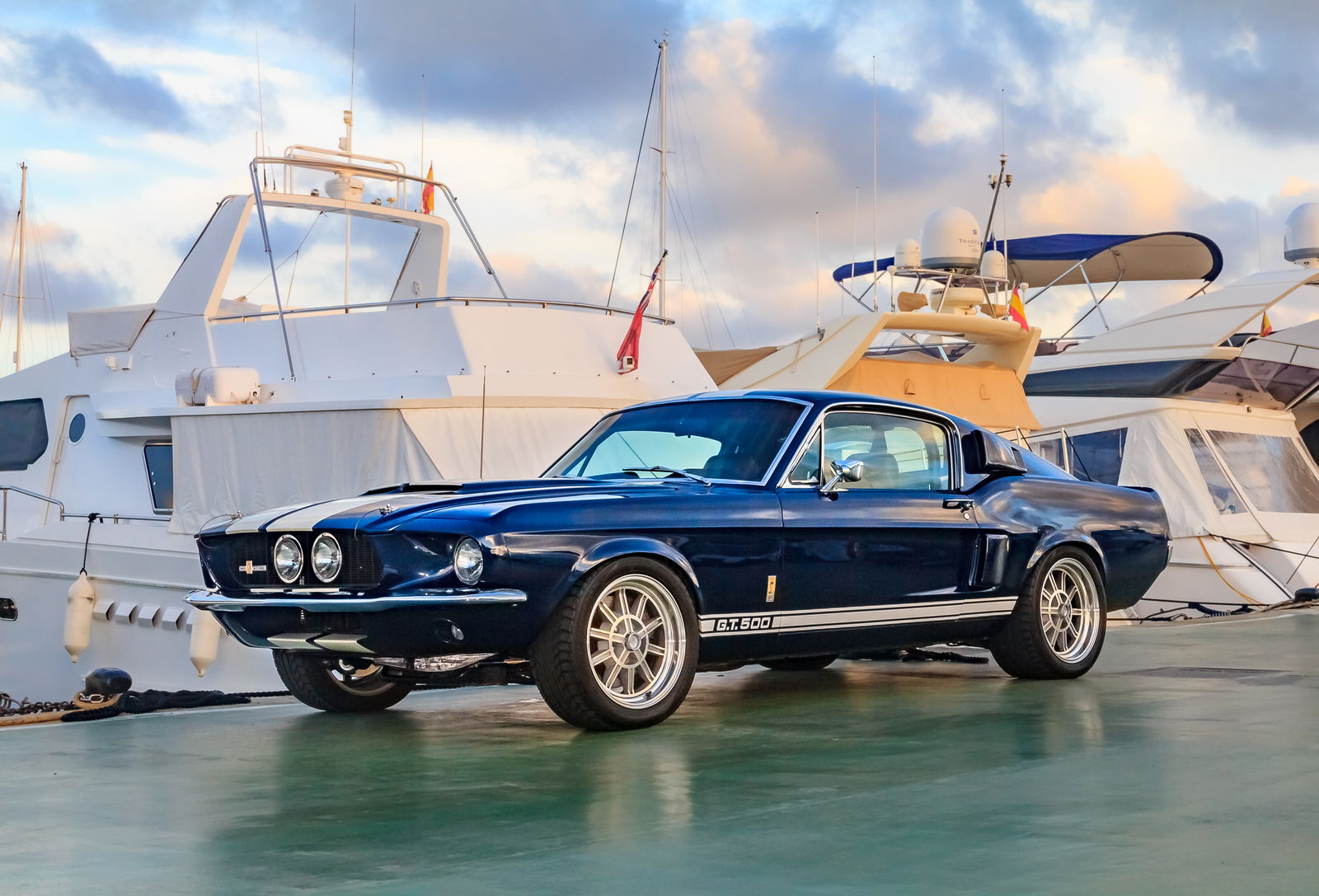 Ein Mustang aus den 60er Jahren in der Farbe Blau steht vor mehreren Yachten