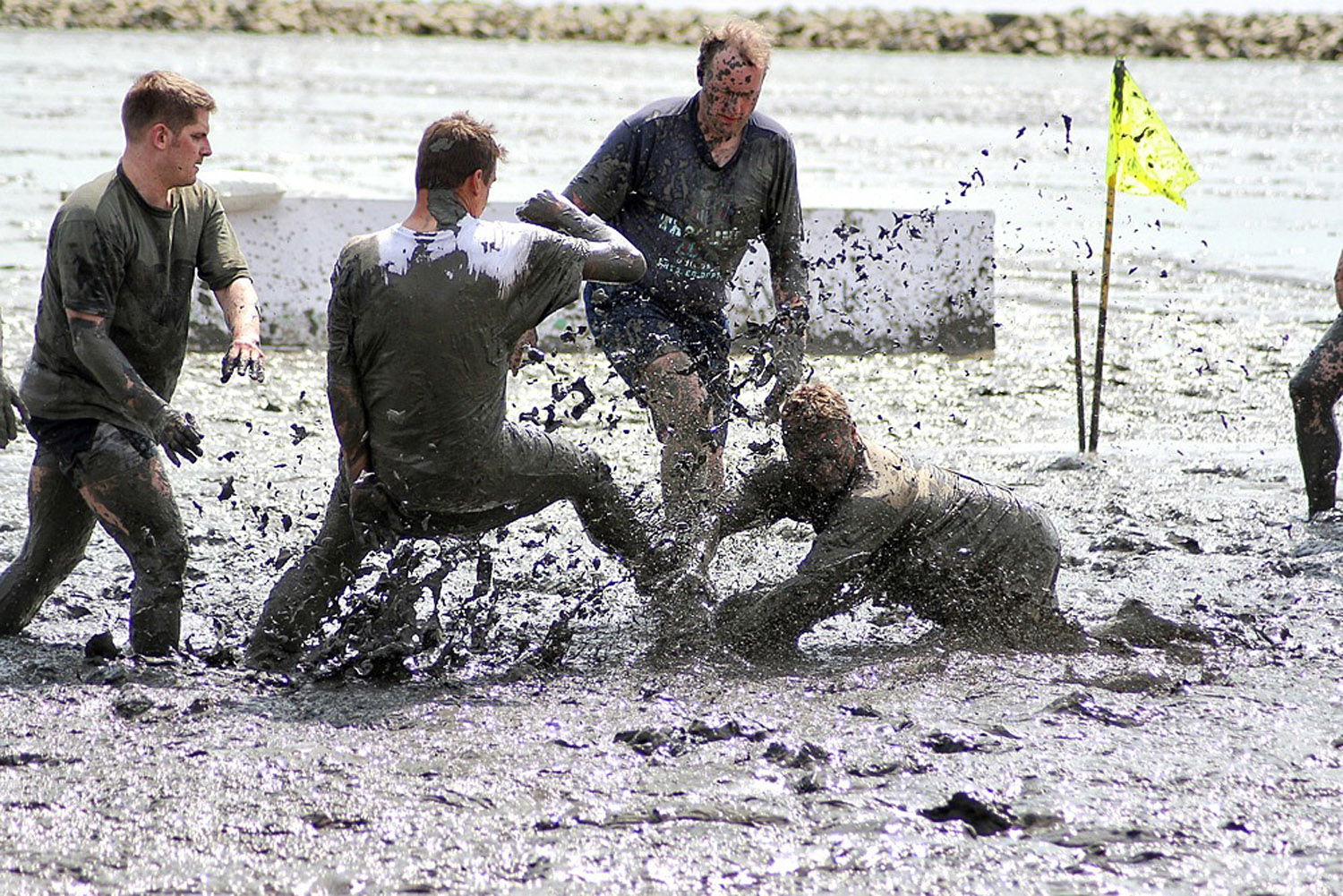 Vier Personen spielen im Matsch des Watt Fußball. Sie sind von oben bis unten mit Matsch beschmiert.