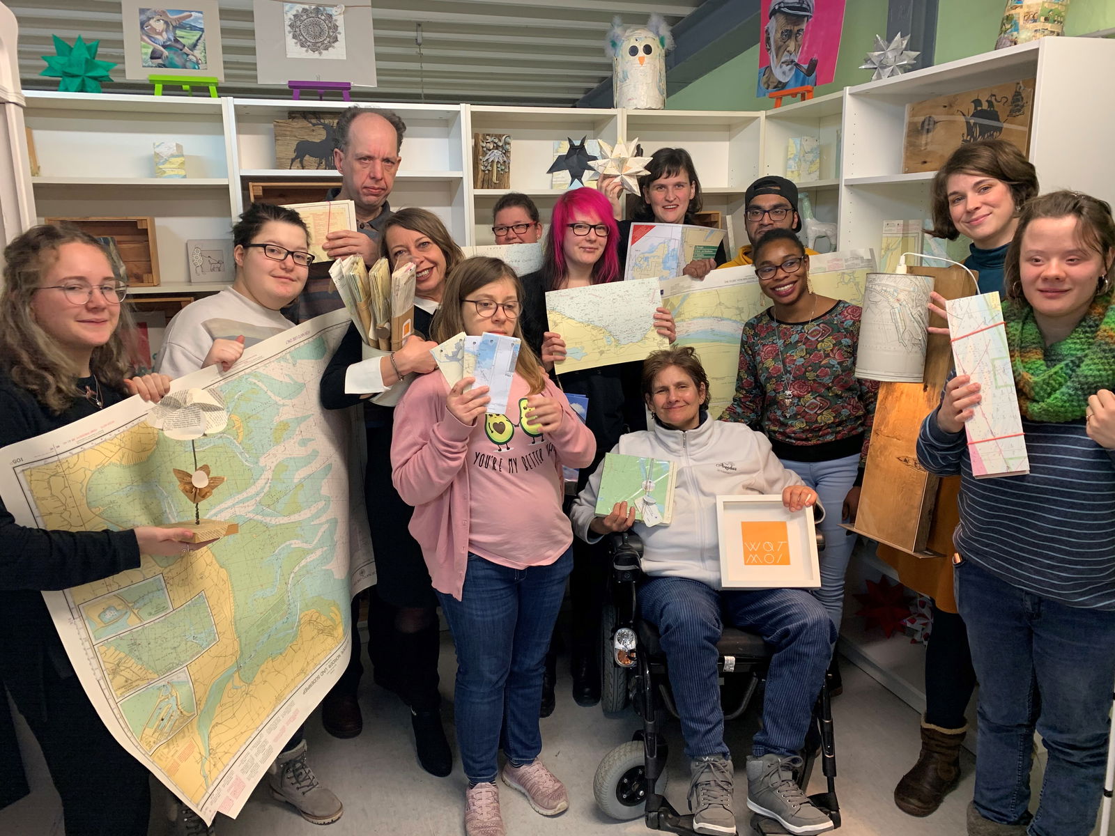 Eine Gruppe Menschen steht vor einem Regal und präsentiert Produkte, die von ihnen aus alten Seekarten hergestellt wurden.