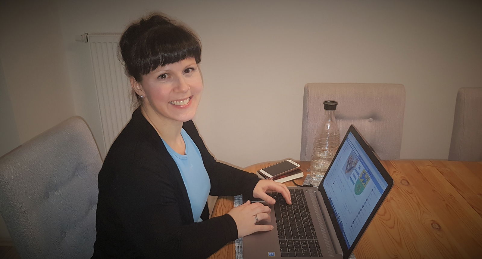 Eine junge Frau sitzt vor einem aufgeklappten Laptop an einem Holztisch.