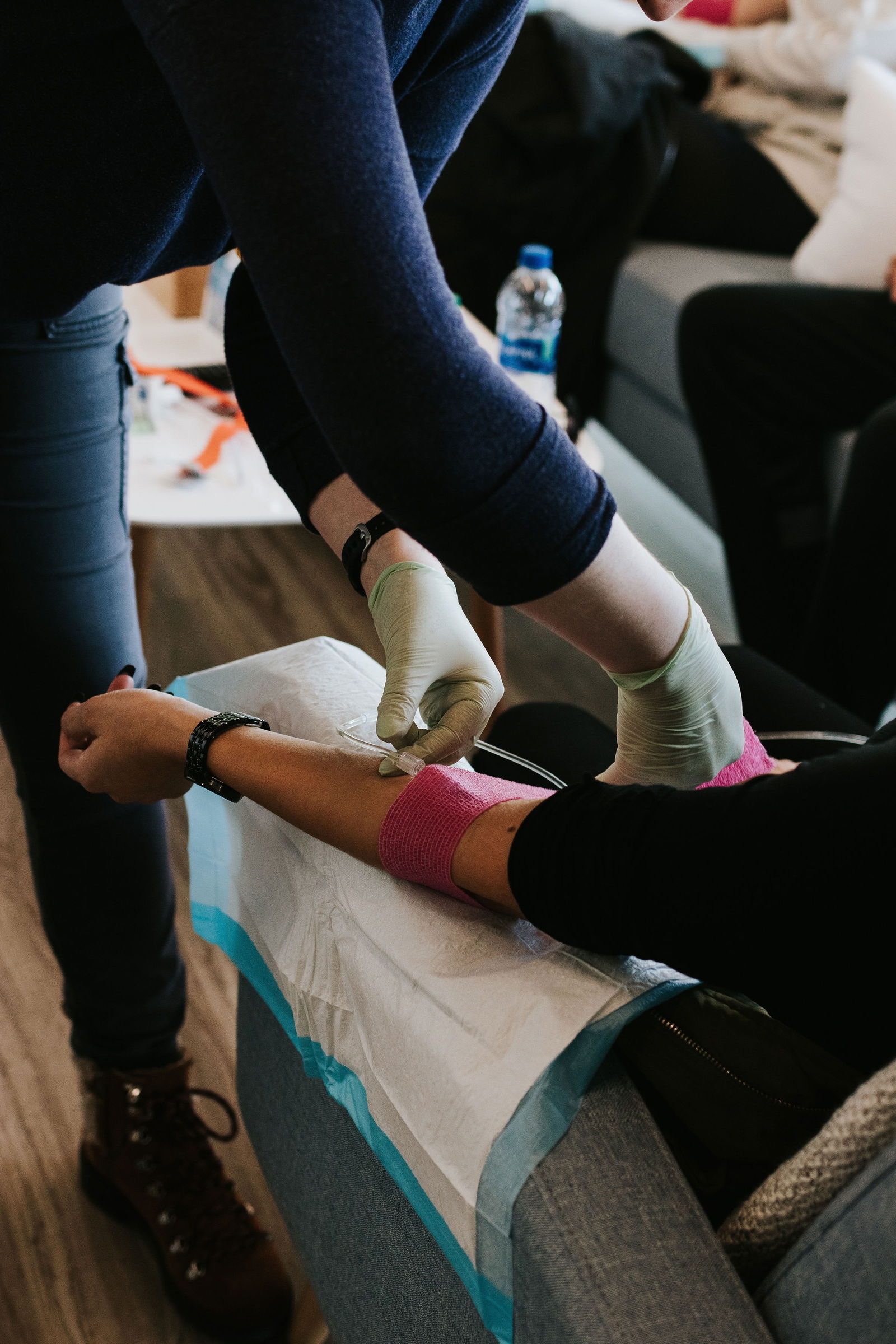 Eine Frau sitzt auf einem Sessel, an ihrem Arm hat eine andere Frau eine Spritze zur Blutabnahme angesetzt.