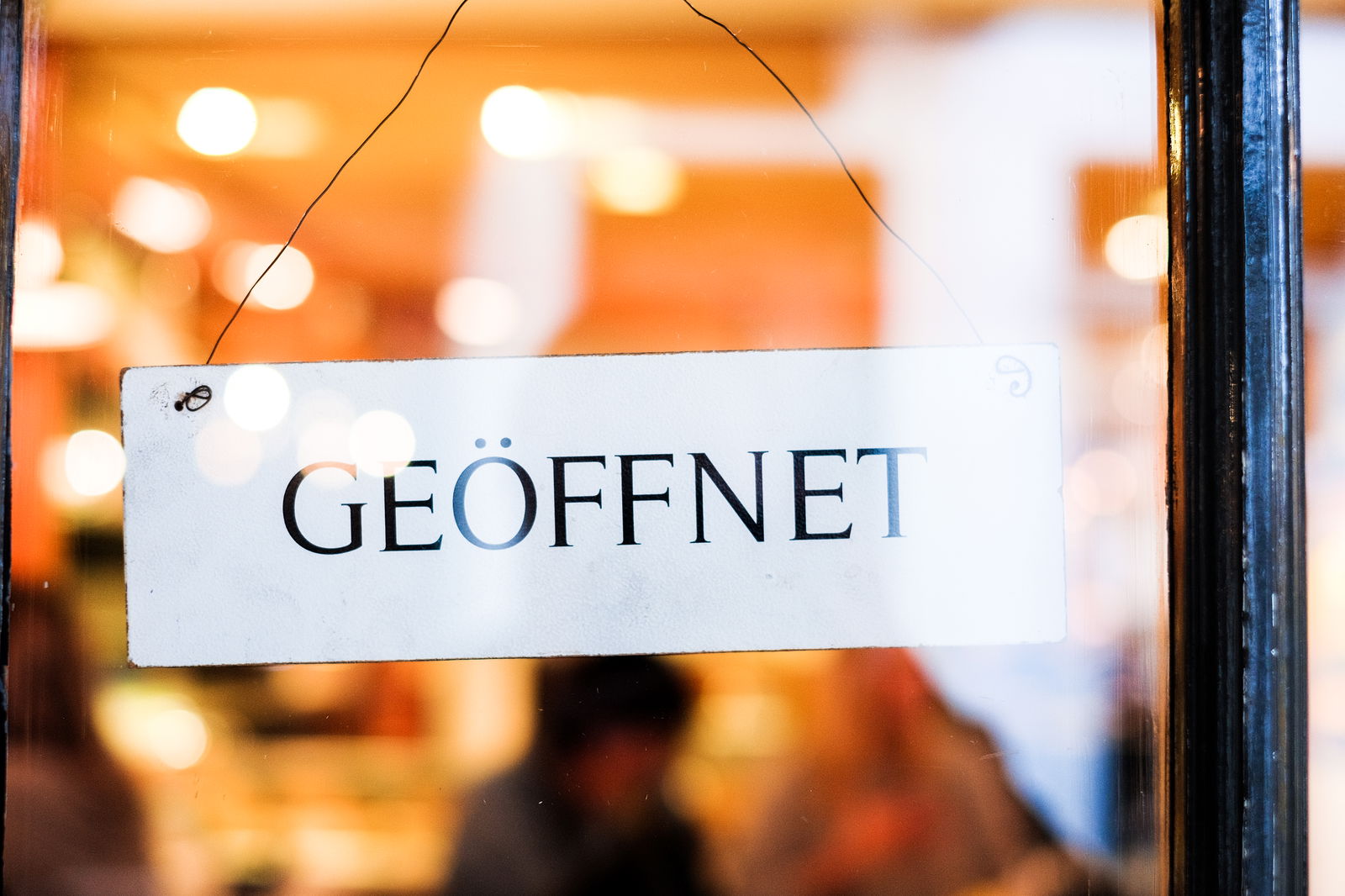 EinSchild mit dem Hinweis geöffnet hängt an einer Glastür.