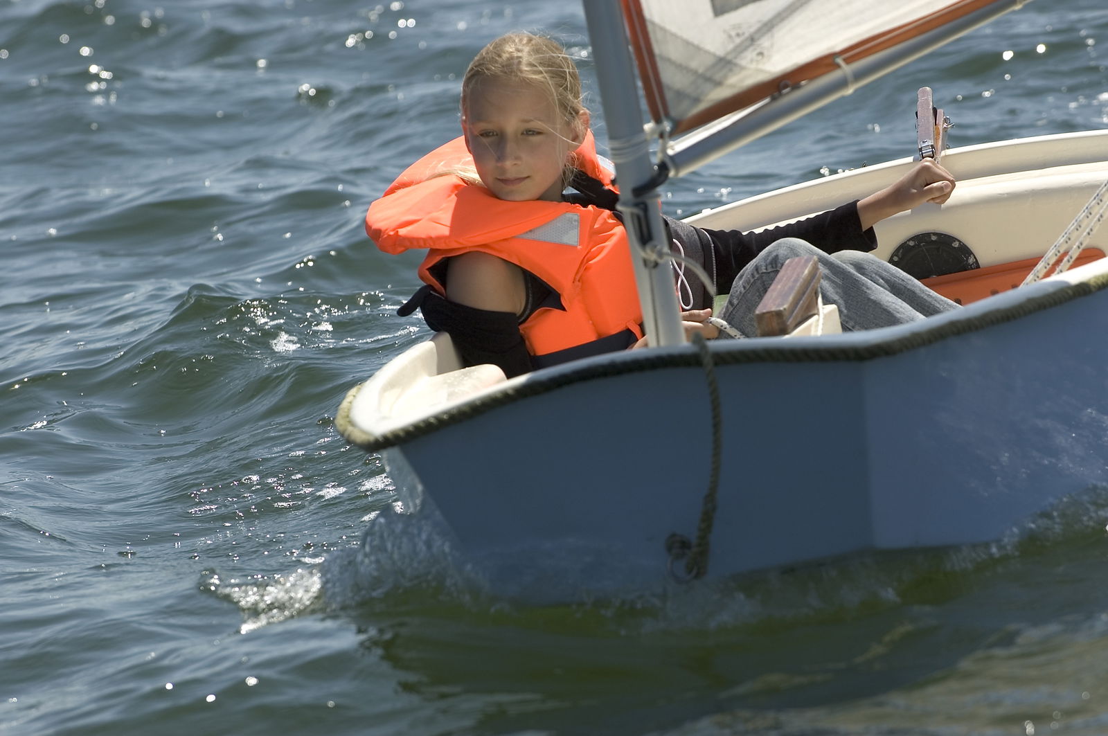Ein Mädchen sitzt in einem Optimisten und segelt auf dem Wasser.