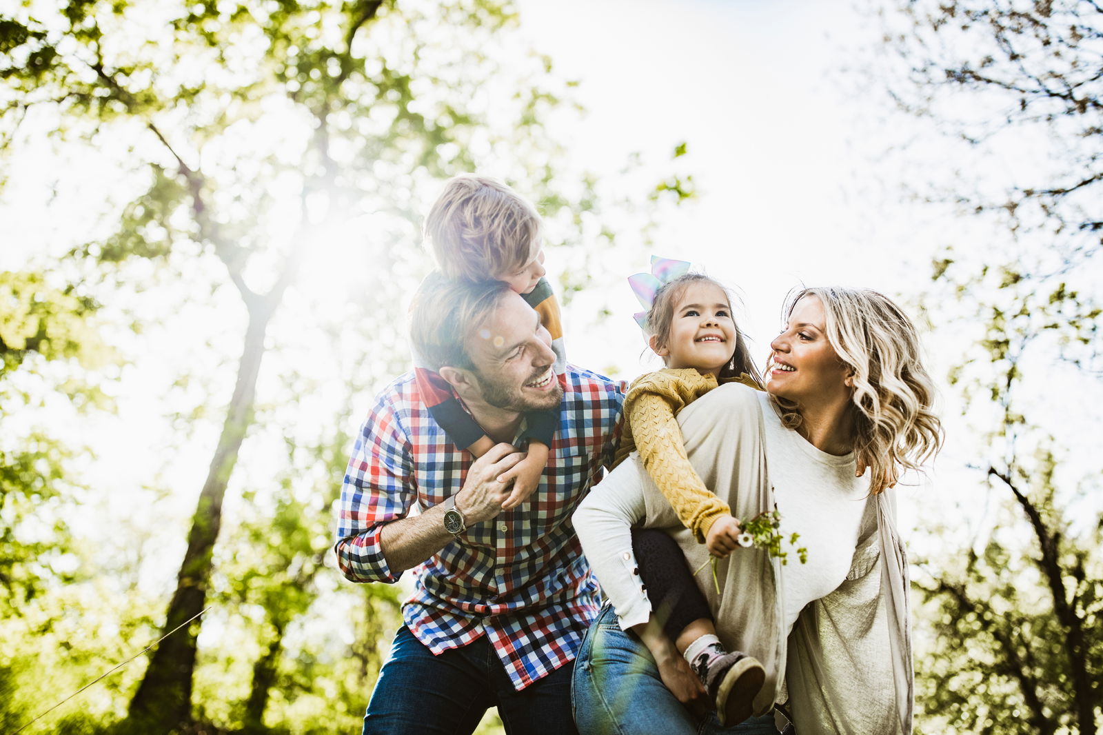 Eine Familie bestehend aus zwei Kindern und zwei Erwachsenen steht in einem Wald und lacht sich an.