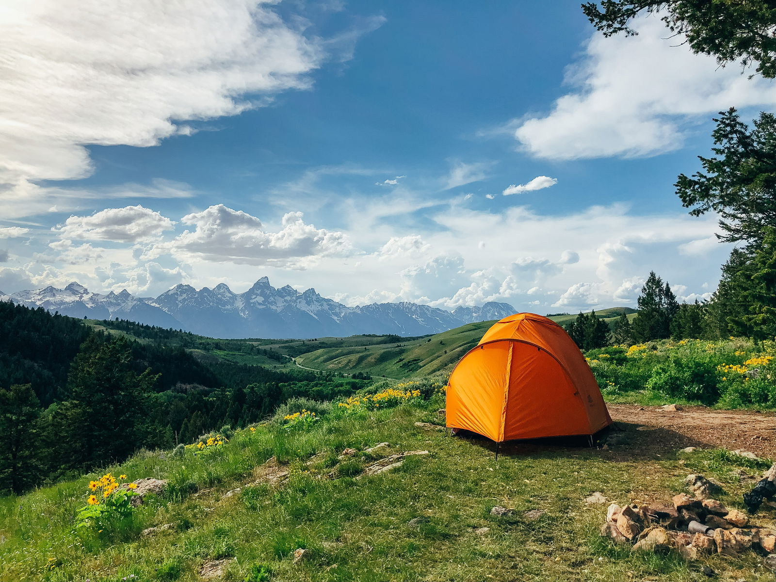 An einem Berghang steht ein orangenes Zelt. Dahinter sieht man ein Bergpanorama.