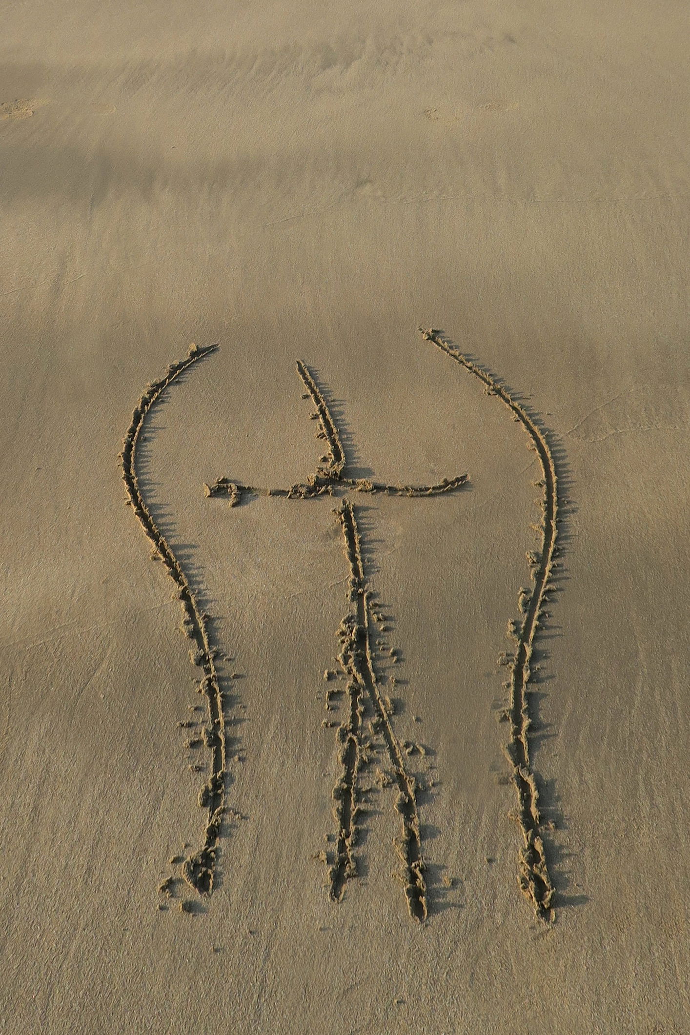 Am Strand im Sand ist das Bild von einem menschlichen Po gemalt.