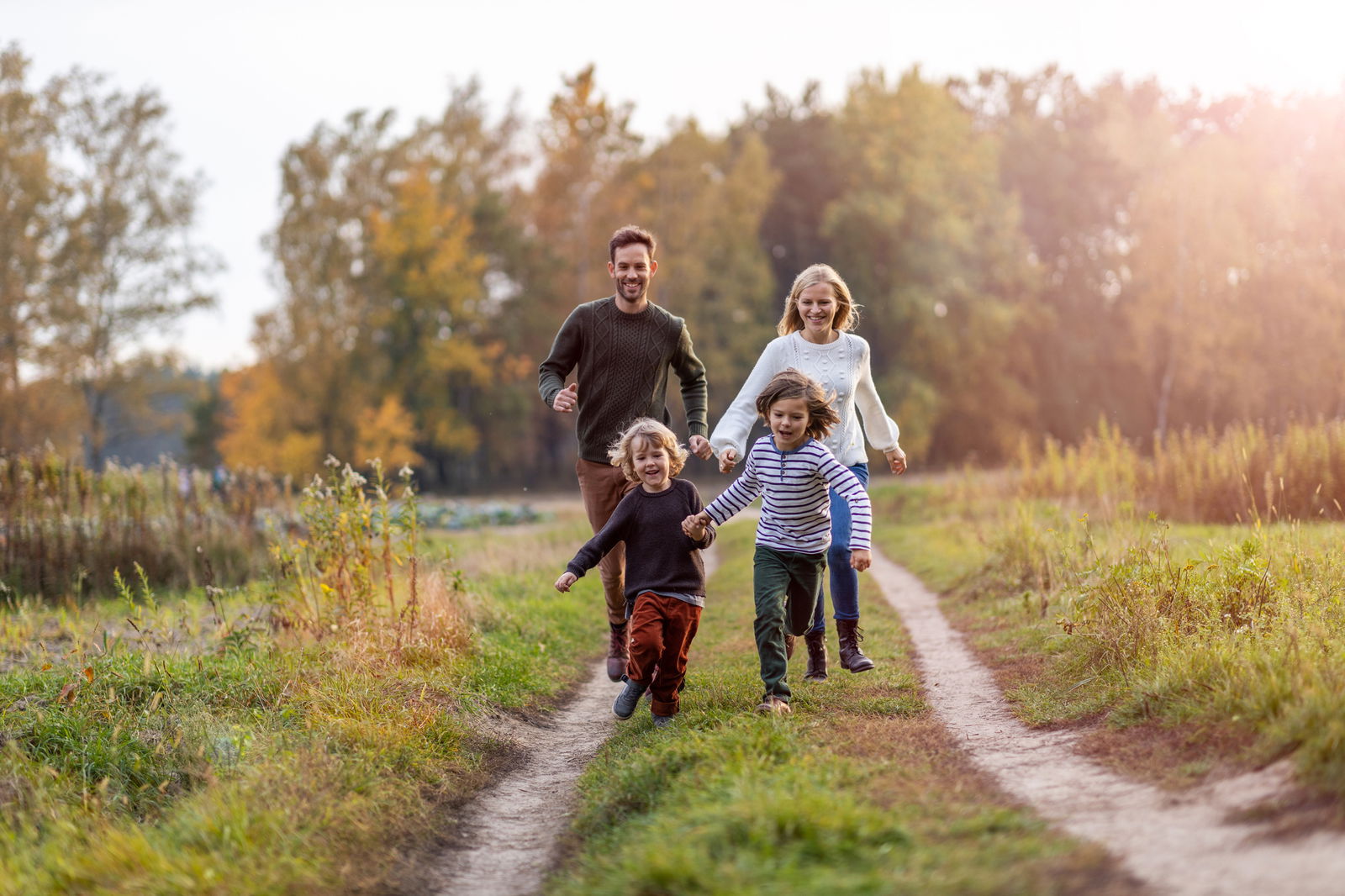 Zwei Erwachsene und zwei Kinder laufen einen Feldweg entlang. Die Bäume und Sträucher im Hintergrund sind herbstlich bunt gefärbt.