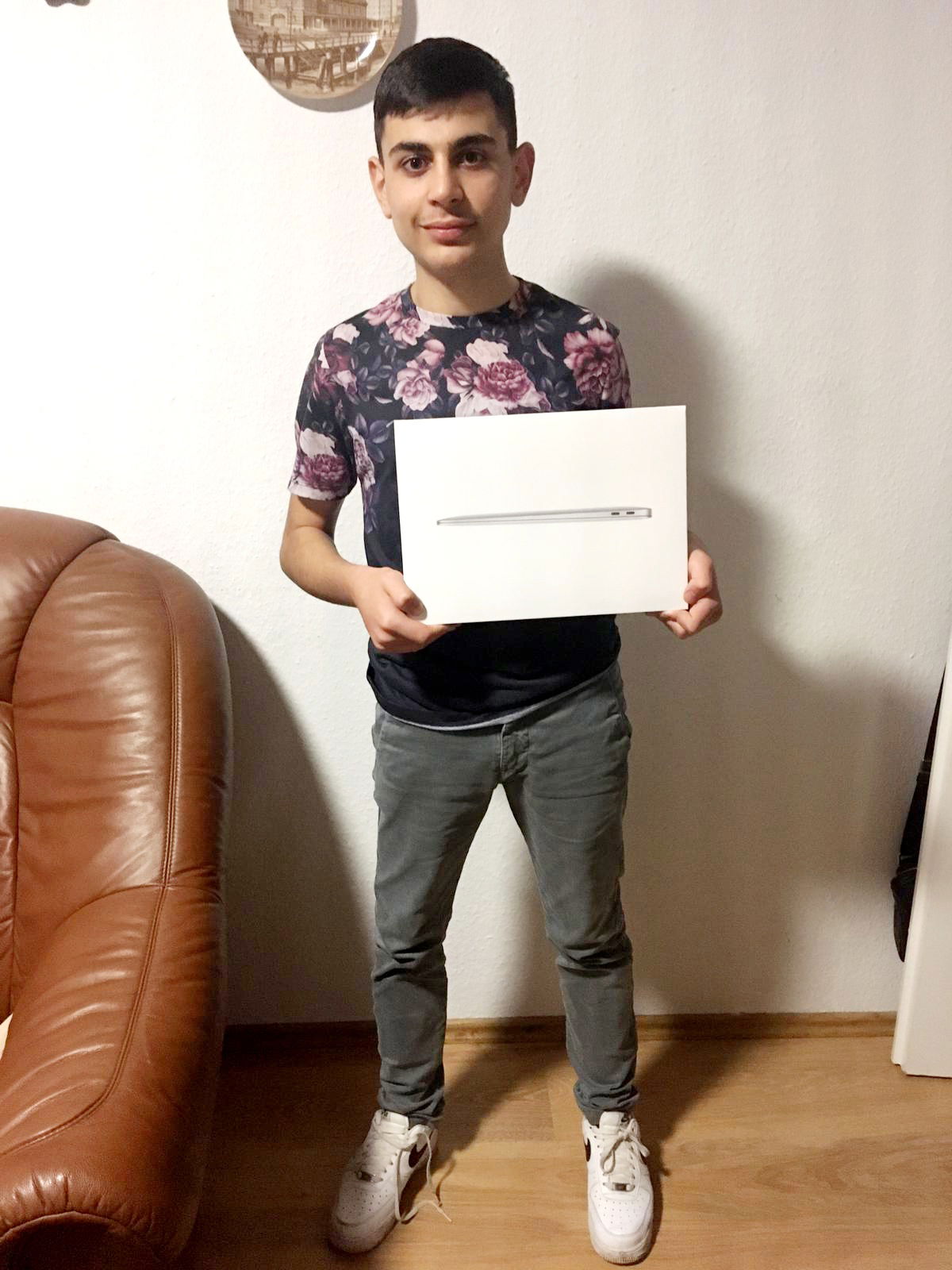 Ein Junge hält einen Laptop-Karton in der Hand und schaut in die Kamera.