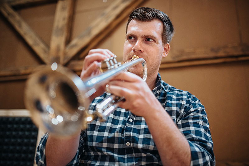 Ein Mann im blau-grün karierten Hemd spielt Trompete 