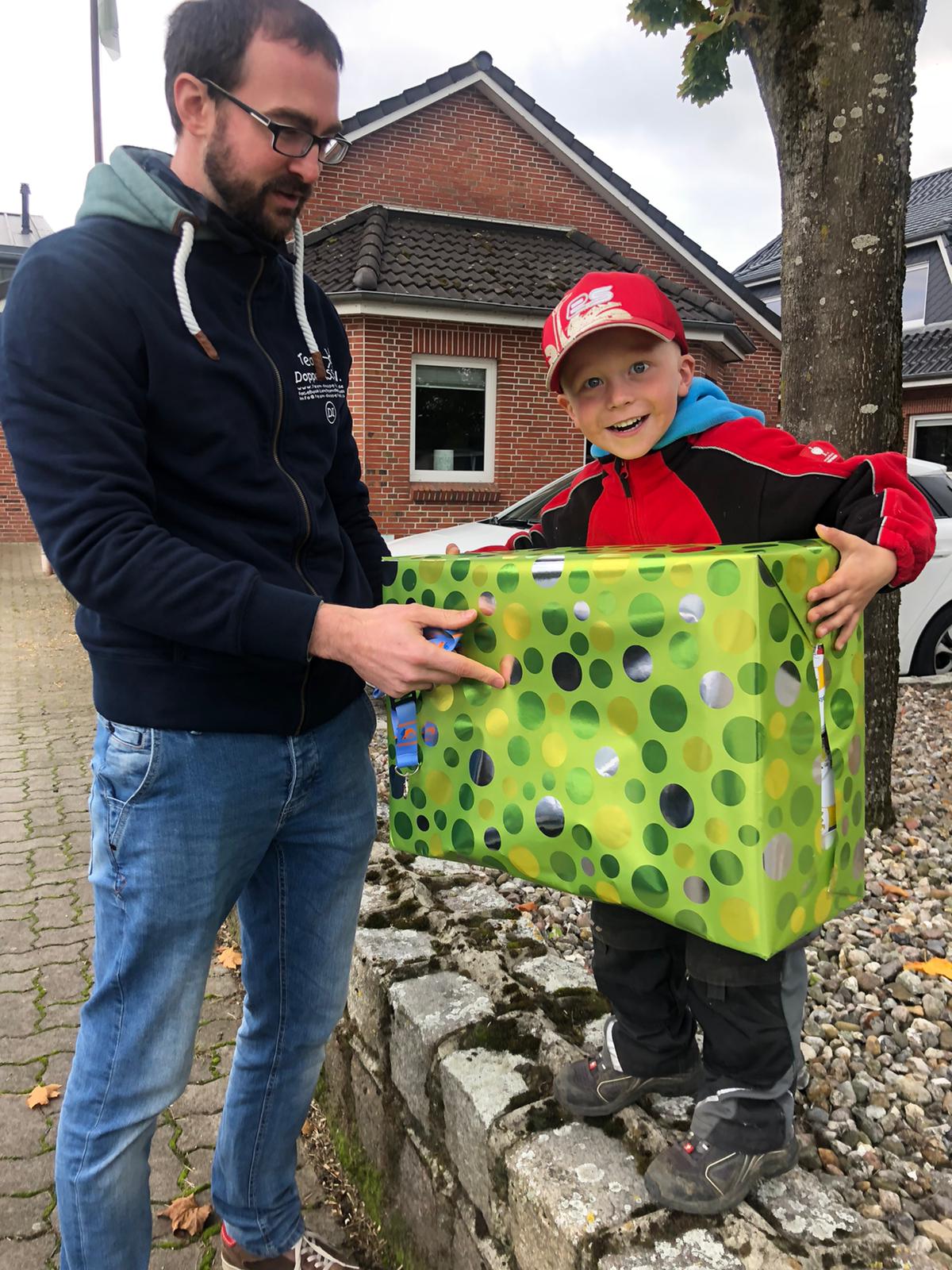 Ein Junge nimmt mit großen Augen ein großes Geschenk von einem Mann entgegen.