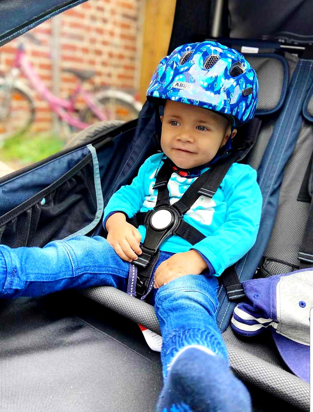 Ein kleiner Junge mit Helm sitzt angeschnallt in einem Fahrradanhänger.
