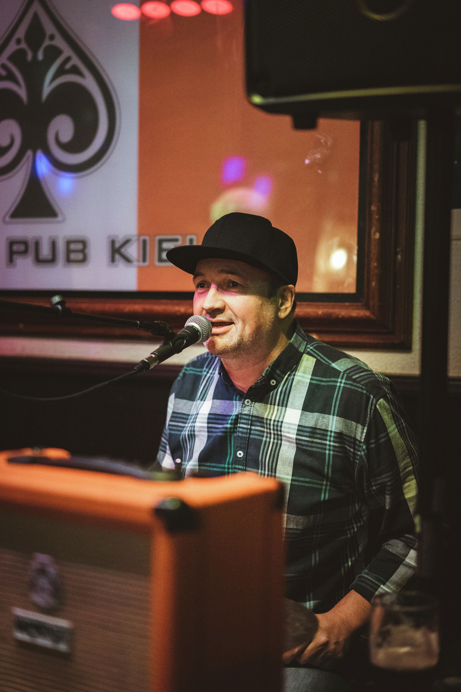 Ein Mann im karierten Hemd und einer schwarzen Cap singt in ein Mikrofon.