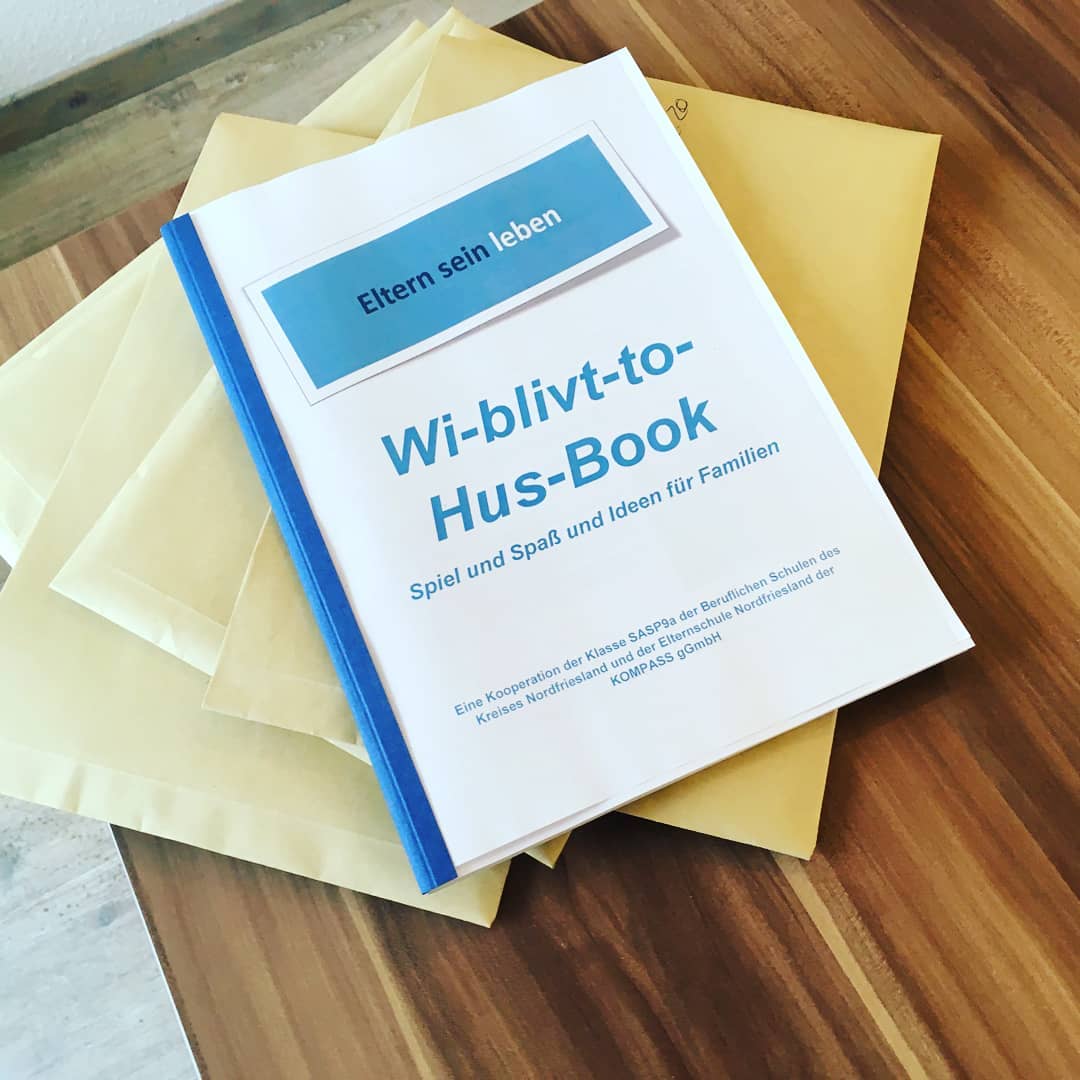 Ein geheftetes Buch mit der Aufschrift "Wi blivt to hus-Book" liegt auf einem Stapel auf einem Tisch.