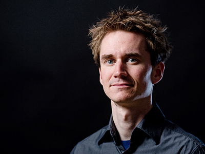 Ein mittelalter, kurzhaariger Mann vor schwarzem Hintergrund schaut ernst in die Kamera.