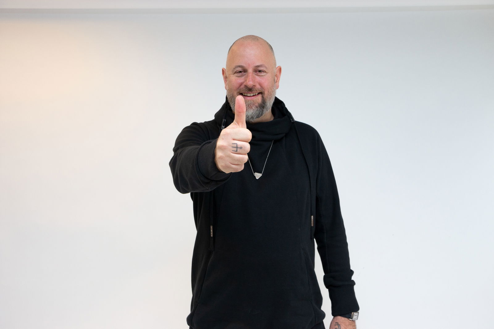 Ein schwarz gekleideter Mann mit Glatze zeigt einen Daumen in die Kamera.