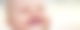 Ein Baby lacht zahnlos und mit zusammengekniffenen Augen in Richtung Kamera.
