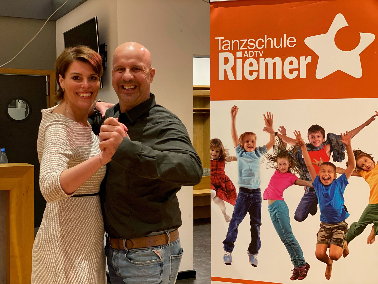 Eine Frau und ein Mann stehen gemeinsam in Tanzpose da und lachen in die Kamera.