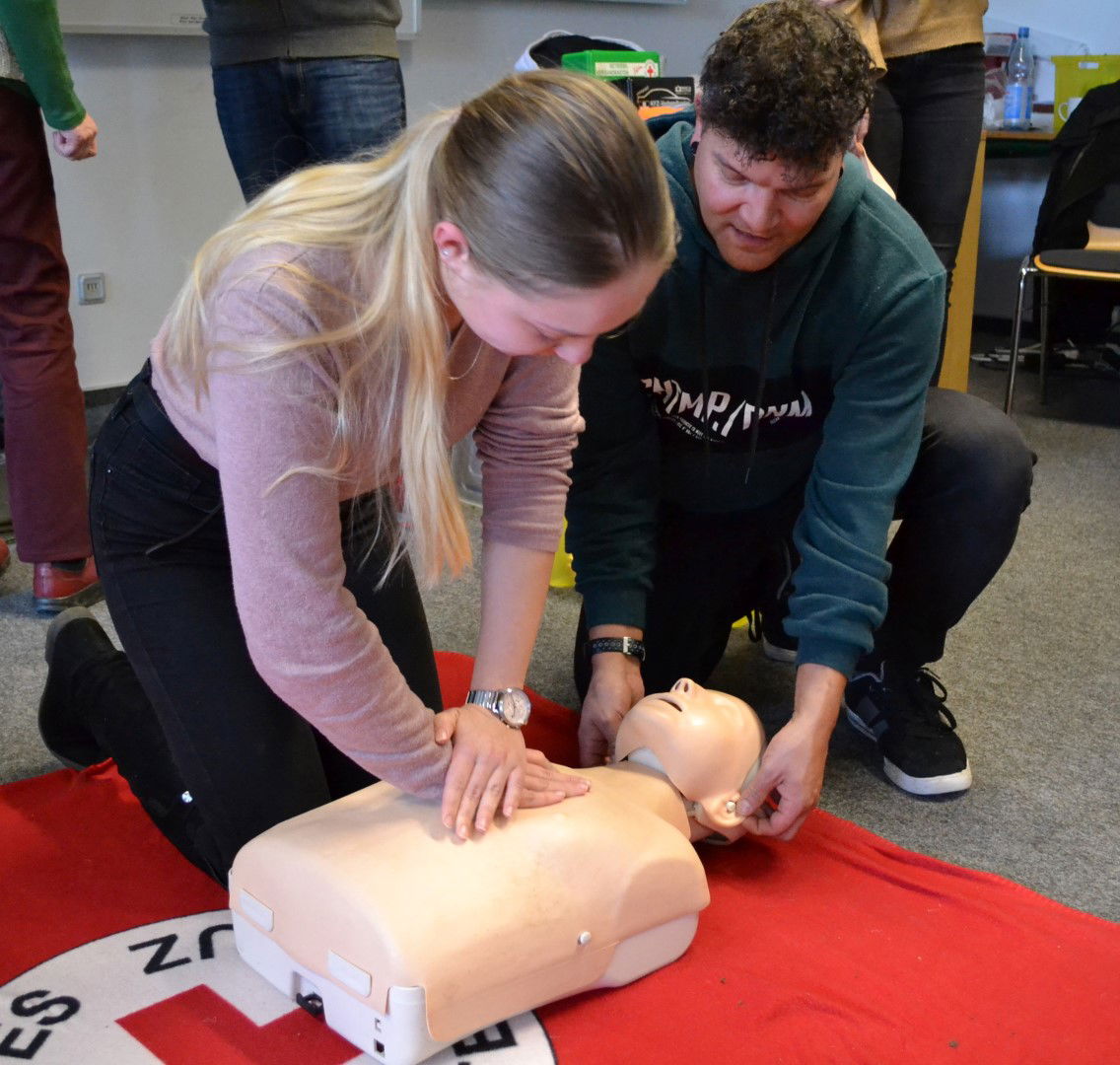 Zwei Menschen knien vor einer Puppe und üben das Widerbeleben