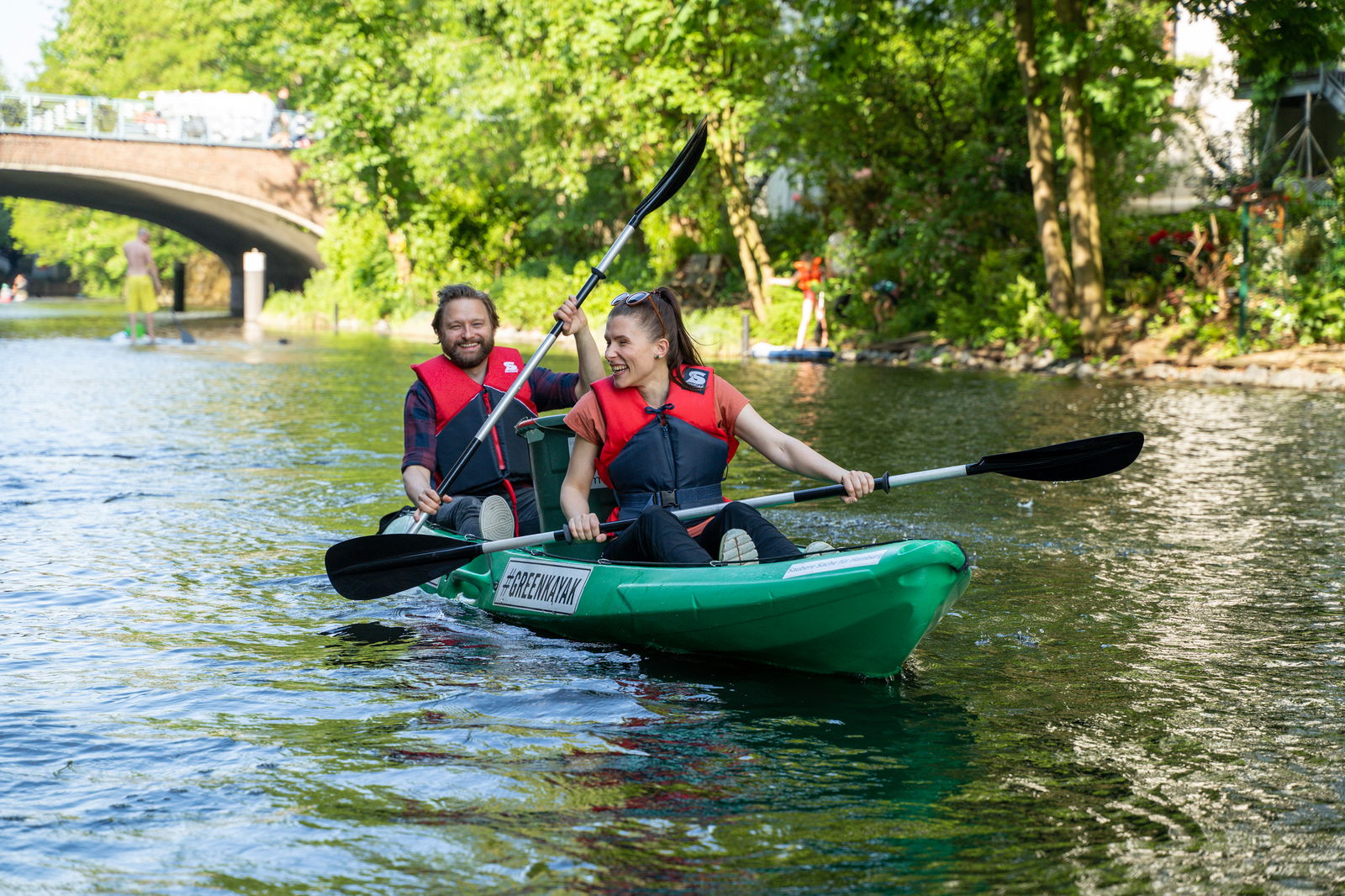 Zwei Menschen in einem grünen Kajak fahren über einen Fluss.