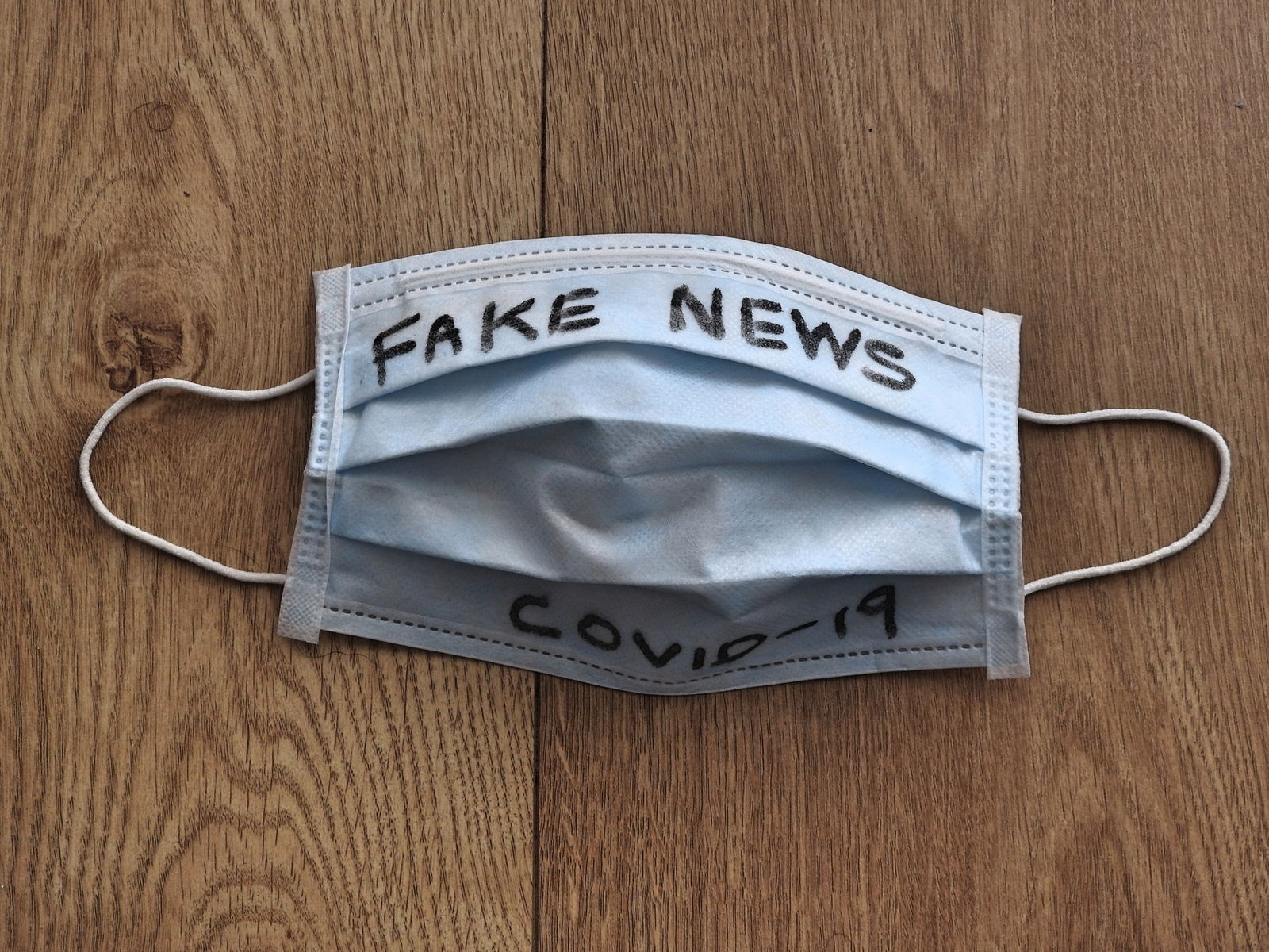 Eine Atemschutzmaske liegt auf einem Tisch und ist mit "Fake News Covid-19" beschriftet.