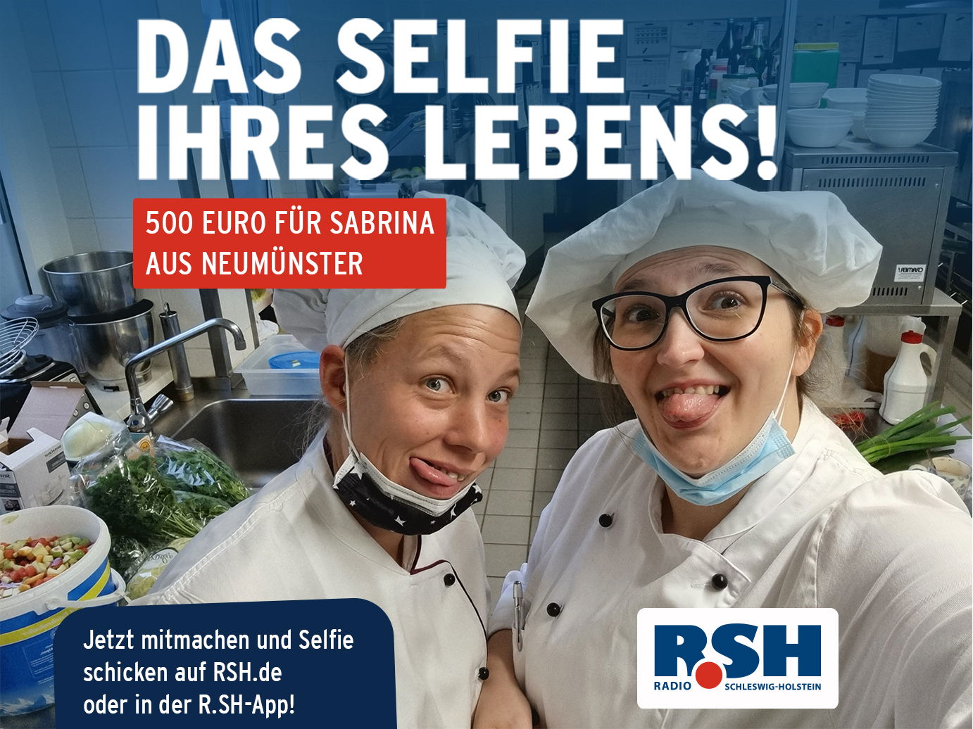 Zwei Frauen in Kochuniform stehen in einer Küche und lachen in die Kamera.