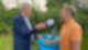 Carsten Kock steht mit R.SH-Mikrofon an einem Tisch. Neben ihm steht in einem orangenen Polohemd Christian Lindner.