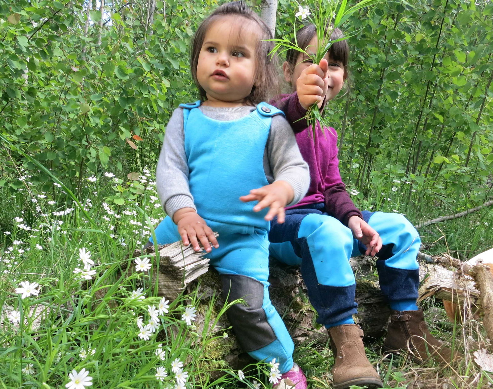 Zwei Kinder in Wollkleidung sitzen im Wald auf einem Baumstamm
