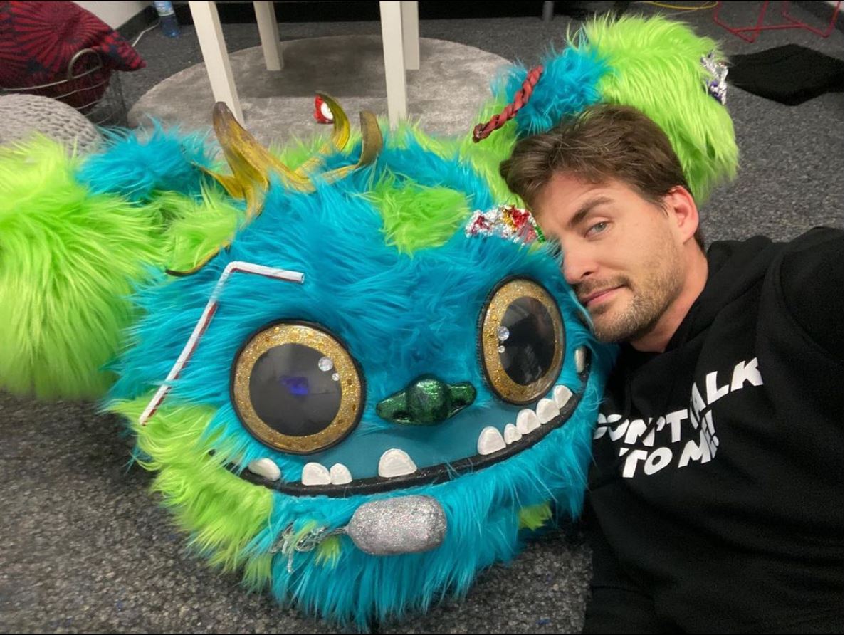 Alexander Klaws liegt neben einer grün-blauen Maske und schaut erschöpft in die Kamera.