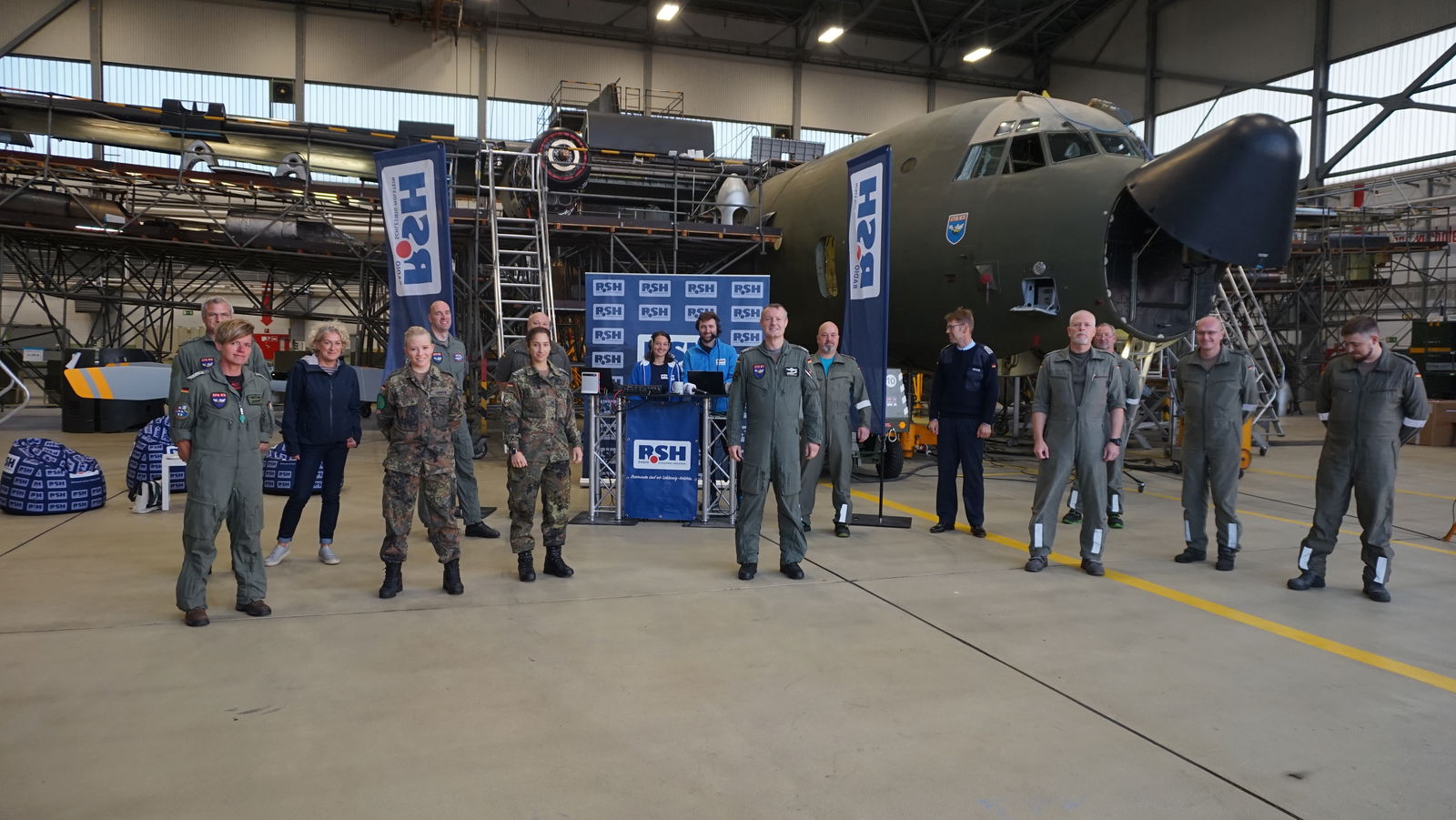 Vor einem großen Flugzeug stehen Menschen in Bundeswehr-Kleidung und zwei Menschen in blauer R.SH-Kleidung.