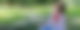 Eine junge Frau sitzt mit Kopfhörern und Handy auf einer grünen Wiese und lacht.