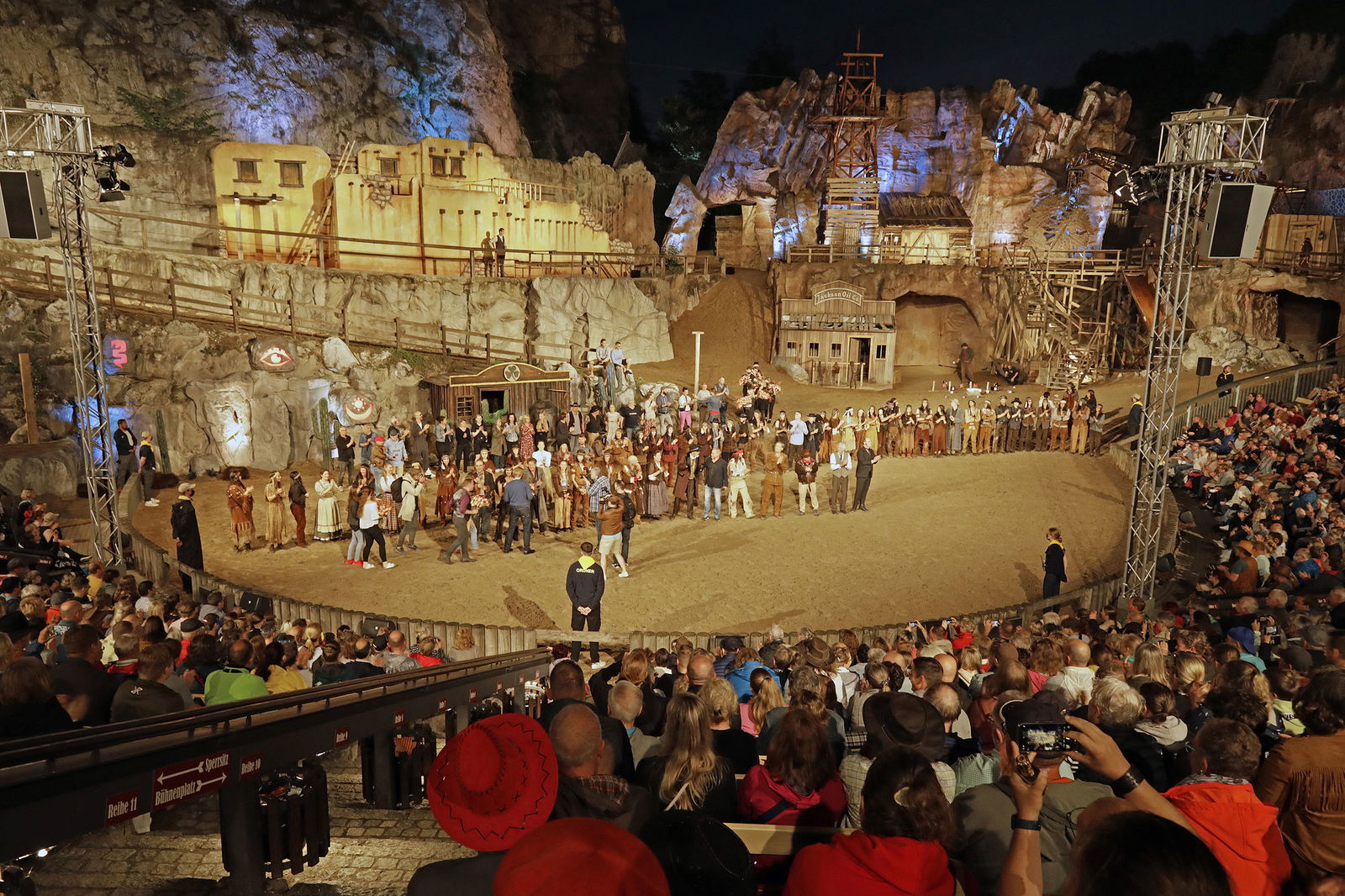Viele Menschen in Kostümen stehen vor einer vollbesetzten Arena.