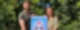 Matze Schmak und Danica Großer stehen gemeinsam auf einer Wiese in sommerlicher Kleidung und halten ein Plakat mit der Aufschrift "Vorsicht Schulkinder!" in die Kamera.
