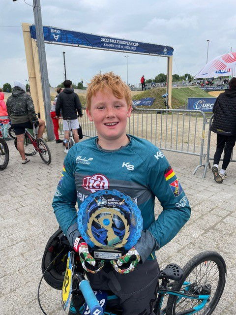 Ein Junge in einem Trikot hält stolz einen Pokal in die Kamera.