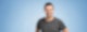 Dominik Feist steht in einem grauen T-Shirt vor blauem Hintergrund und lächelt in die Kamera.