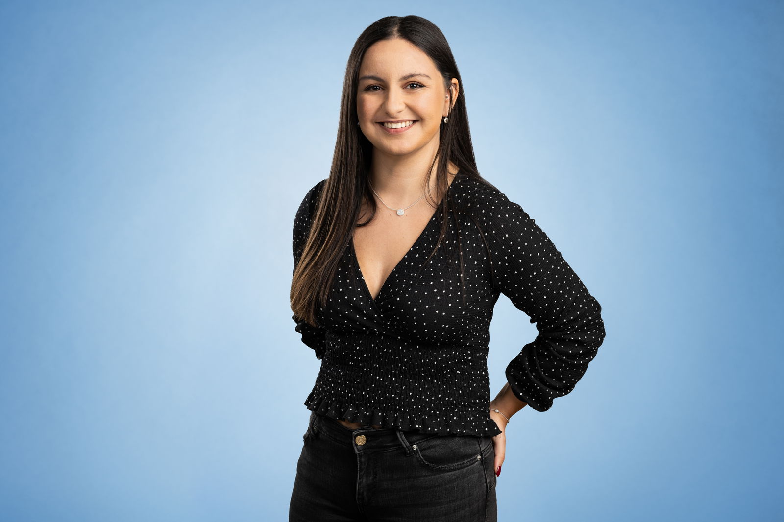 Melissa Yilmaz steht in einem schwarzen Oberteil vor blauem Hintergrund und lächelt in die Kamera.