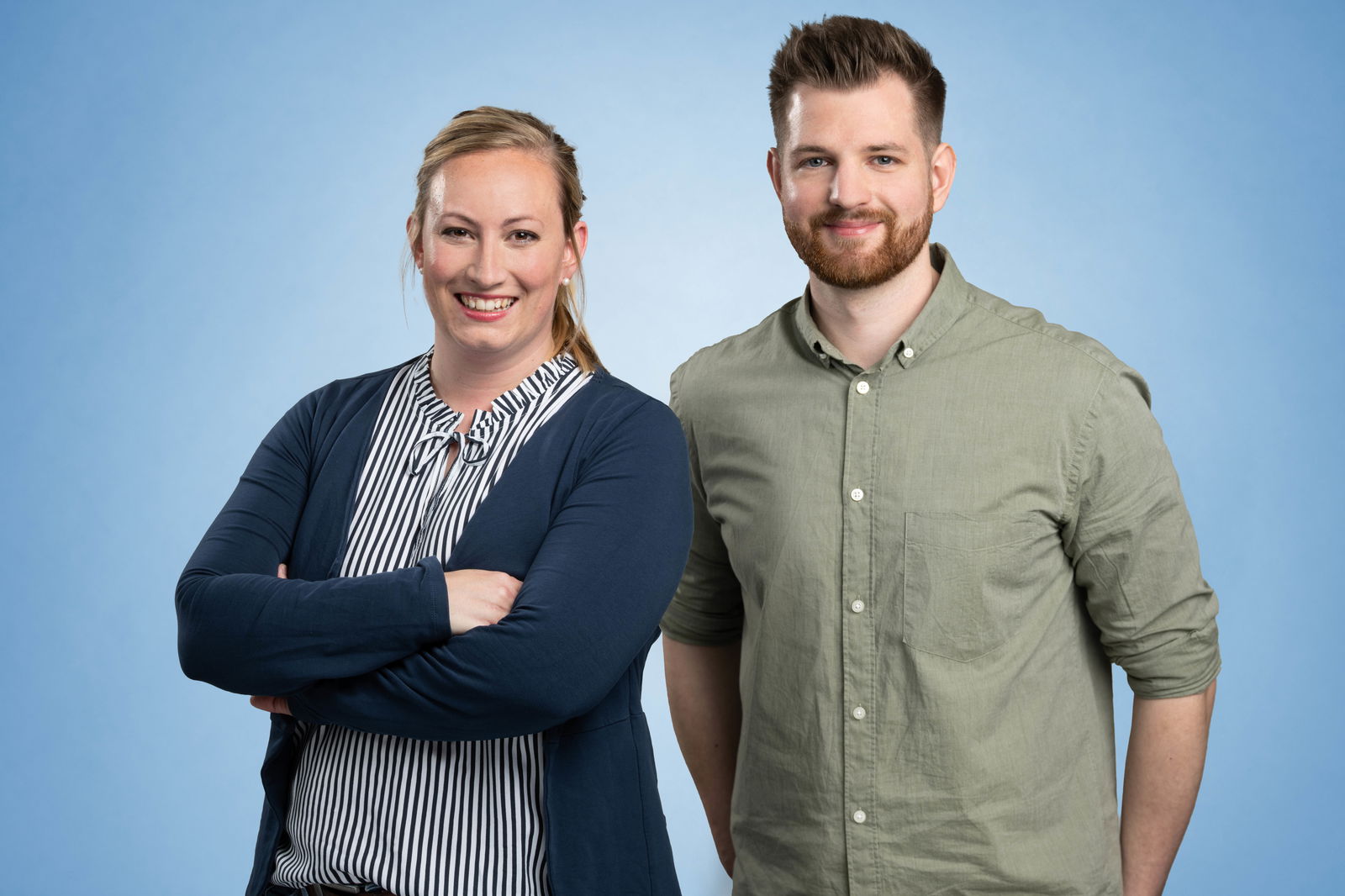 Sharon Heyn und Maik Brockstedt stehen vor einem blauen Hintergrund und lächeln in die Kamera.