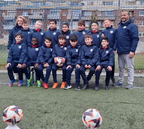 Eine Fußballmannschaft mit Trainingsjacken steht mit Trainern vor einem Fußballtor.
