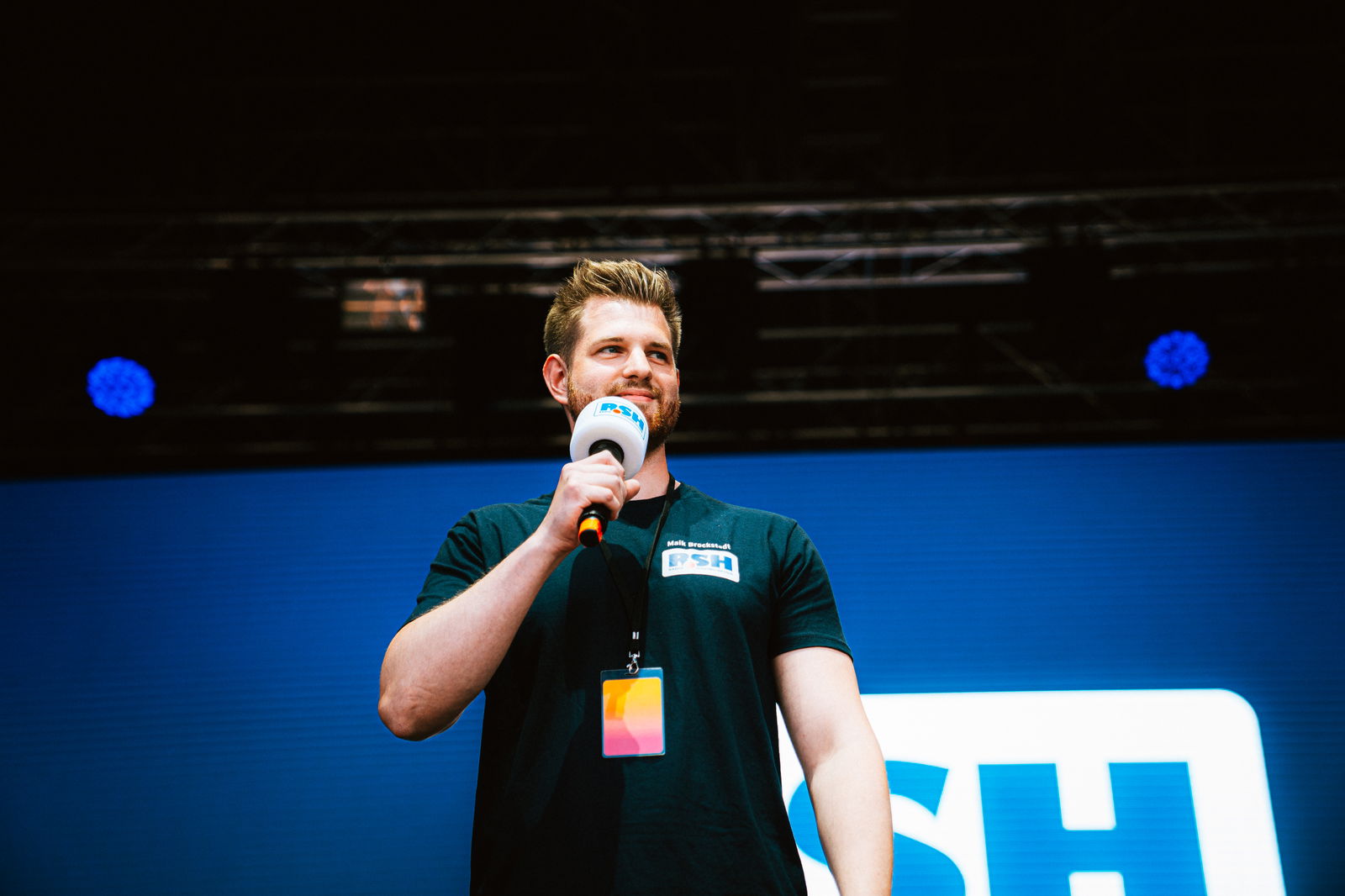 Maik Brockstedt steht auf einer Bühne und hält ein Mikrofon in der Hand