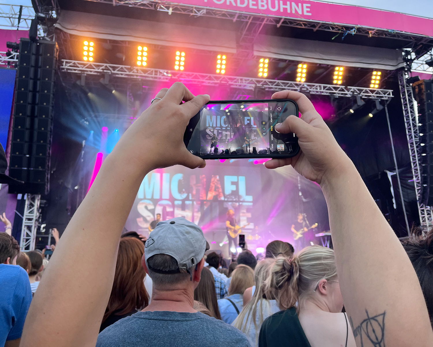 Eine Frau hält ein Handy vor einer Bühne in die Luft