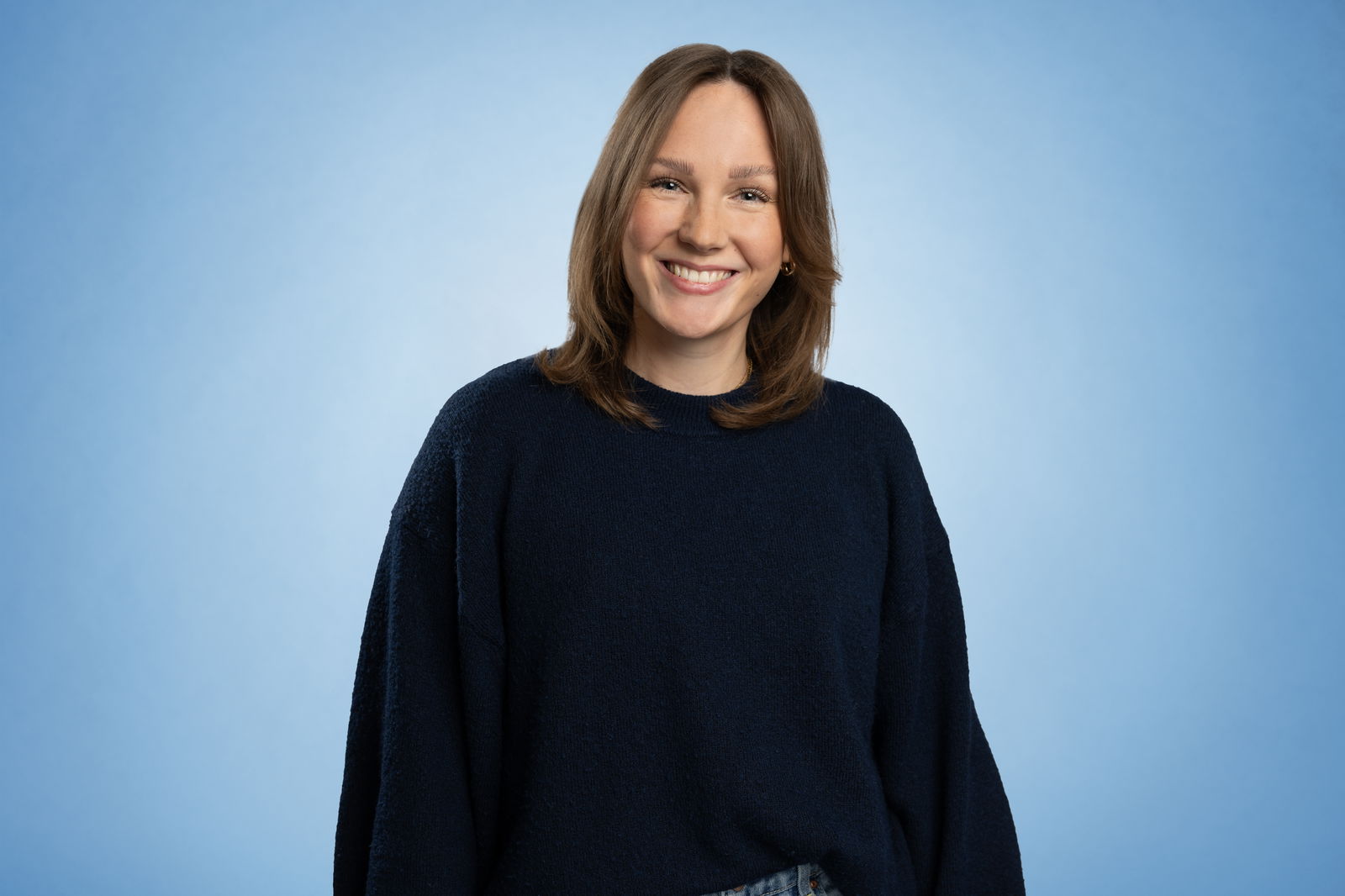 Alicia Janson steht vor einem blauen Hintergrund und lächelt in die Kamera